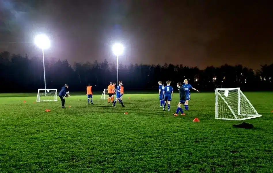 Children playing soccer on a lit field.